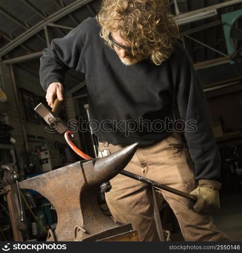 Metalsmith shaping metal on anvil.