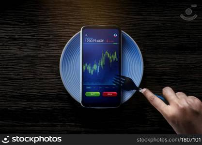 Metaphor Conceptual Photo. Person Using Fork to Eating Stock Market Graph on Mobile Phone. Online Investment in Daily Life. Lifestyle of Modern People. Table Top View