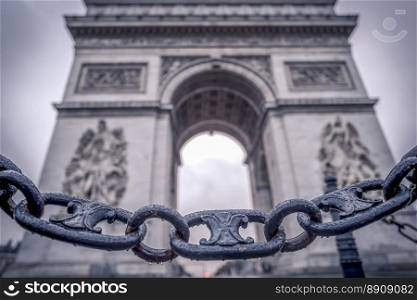 Metaphoric image with chain links sprinkled with rain drops in the foreground and the Arc de triumph on the background, in Paris, France.