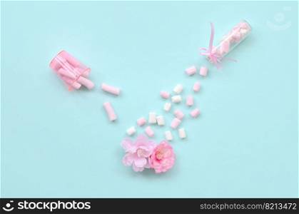 Metaphorical concept of care for flowers. Pink flower sprayed with marshmallows from small transparent tanks on a pastel blue background. Minimal flat lay composition. Top view. Concept of care for flowers. Pink flower sprinkled with marshmallows