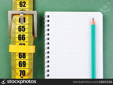 meter belt slimming and notepad with a pencil on the green background