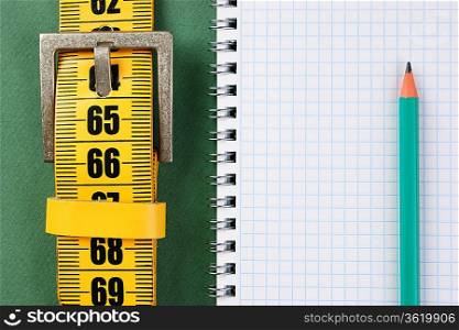 meter belt slimming and notepad with a pencil on the green background