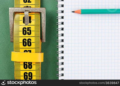 meter belt slimming and notepad with a pencil on the green background