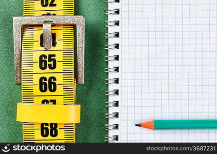 meter belt slimming and notepad with a pencil on the green background