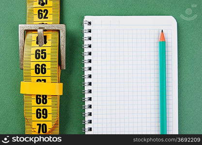 meter belt slimming and notepad with a pencil on the green background