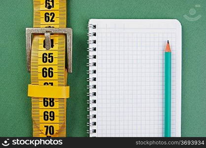 meter belt slimming and notepad with a pencil on the green background