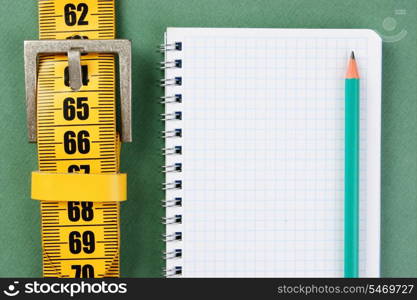 meter belt slimming and notepad with a pencil on the green background