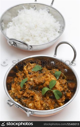 Methi murgh - chicken cooked with fresh fenugreek leaves - in a kadai, or karahi, traditional Indian wok, over white, garnished with fenugreek leaves, next to a bowl of basmati rice and seen from above