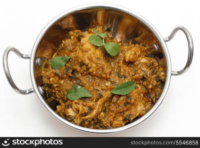 Methi murgh - chicken cooked with fresh fenugreek leaves - in a kadai, or karahi, traditional Indian wok, over white, garnished with fenugreek leaves and seen from above