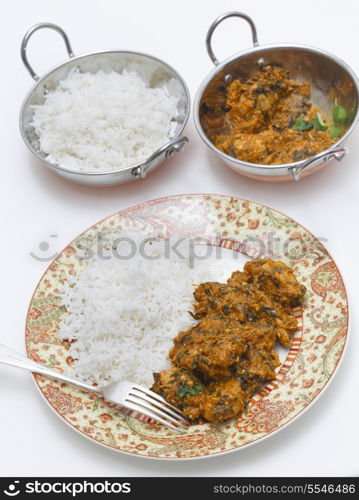Methi murgh - chicken cooked with fresh fenugreek leaves - served on a plate with rice with the curry sauce behind, in a kadai, or karahi, traditional Indian wok, next to a bowl of basmati rice