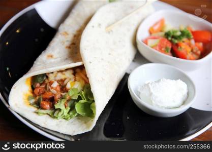 Mexican burritos on a plate with tomato salad