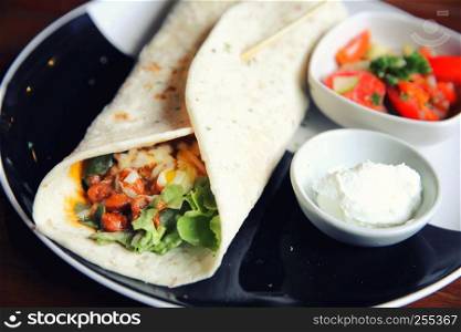 Mexican burritos on a plate with tomato salad