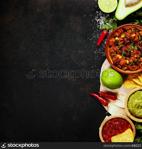 Mexican food concept: tortilla chips, guacamole, salsa, chilli with beans and fresh ingredients over vintage rusty metal background. Top view