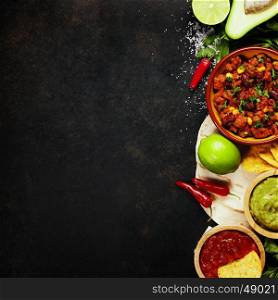 Mexican food concept: tortilla chips, guacamole, salsa, chilli with beans and fresh ingredients over vintage rusty metal background. Top view