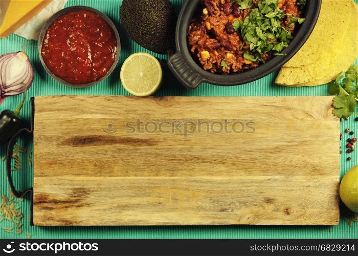 Mexican food concept: tortilla chips, guacamole, salsa, chilli with beans and fresh ingredients over vintage background. Top view