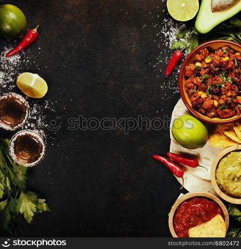 Mexican food concept: tortilla chips, guacamole, salsa, chilli with beans, tequila shots and fresh ingredients over vintage rusty metal background. Top view