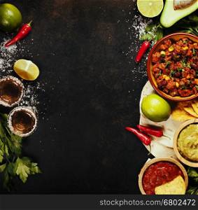 Mexican food concept: tortilla chips, guacamole, salsa, chilli with beans, tequila shots and fresh ingredients over vintage rusty metal background. Top view