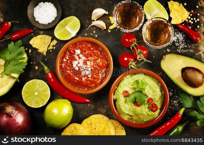 Mexican food concept: tortilla chips, guacamole, salsa, tequila shots and fresh ingredients over vintage rusty metal background. Top view