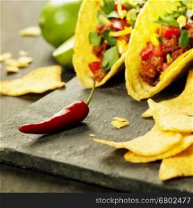 Mexican nachos chips and tacos with meat, beans and salsa on rustic background
