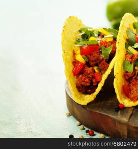 Mexican nachos chips and tacos with meat, beans and salsa on rustic background