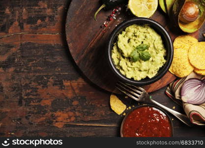 Mexican nachos chips with homemade fresh guacamole sauce and salsa over old background. Top view. Mexican food concept