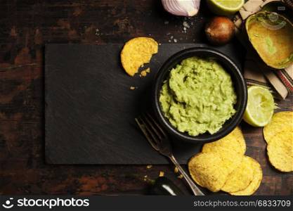 Mexican nachos chips with homemade fresh guacamole sauce on rustic background. With space for text