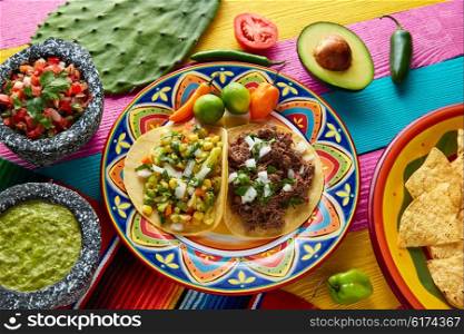 Mexican platillo tacos of barbacoa and vegetarian with sauces and colorful table