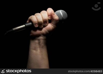 Microphone clinched firmly in male fist on a black background.