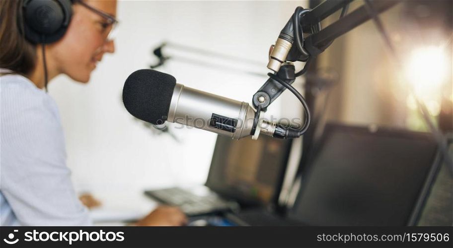 Microphone in a podcasting studio, young host and the broadcasting equipment in the background. Microphone in a podcasting studio, host and the broadcasting equipment in the background