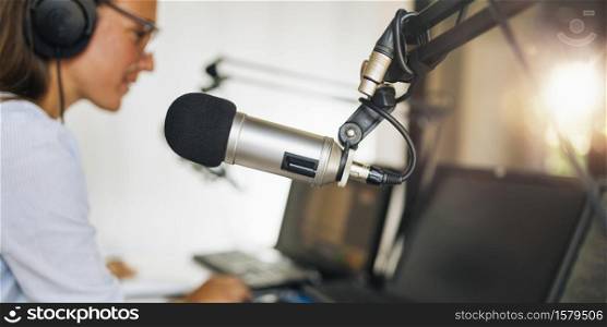 Microphone in a podcasting studio, young host and the broadcasting equipment in the background. Microphone in a podcasting studio, host and the broadcasting equipment in the background