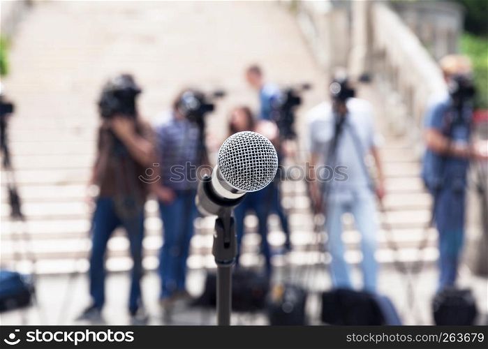 Microphone in focus against blurred camera operators and journalists at news conference