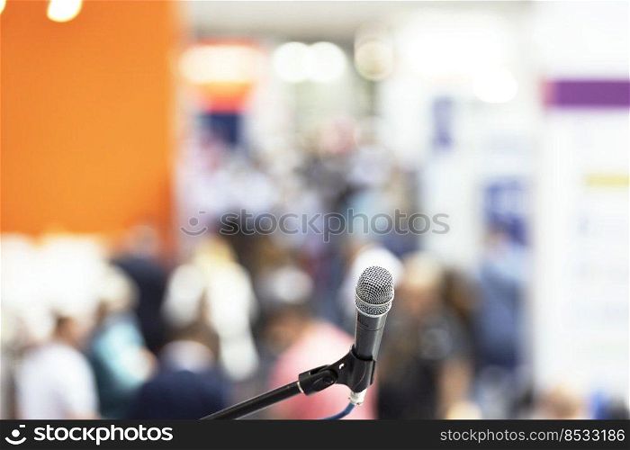 Microphone in focus against blurred crowd of people. Public speaking concept.
