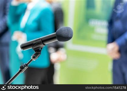 Microphone in focus against blurred people at news or press conference. Public relations - PR concept.