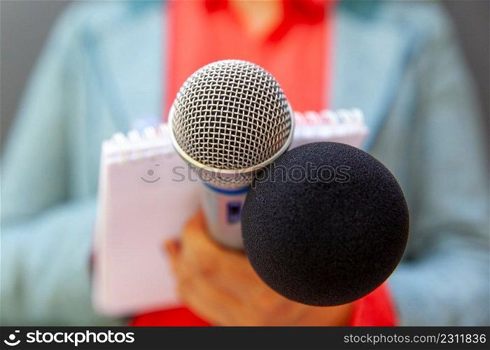 Microphone in the focus, blurred female reporter at press conference or media event writing notes