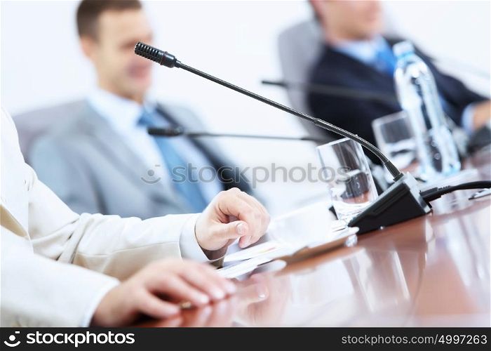 Microphone on table at conference. Image of microphone standing on table at conference against defocused background of two businessmen