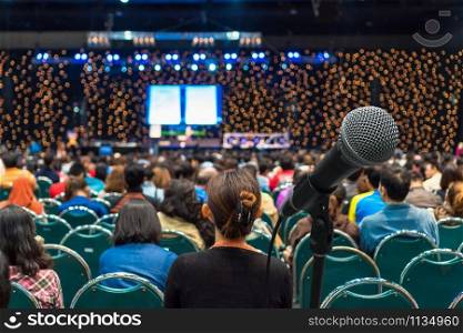 Microphone over the Rear view of Audience in the conference hall or seminar meeting which have Speakers on the stage background, Business meeting and education concept