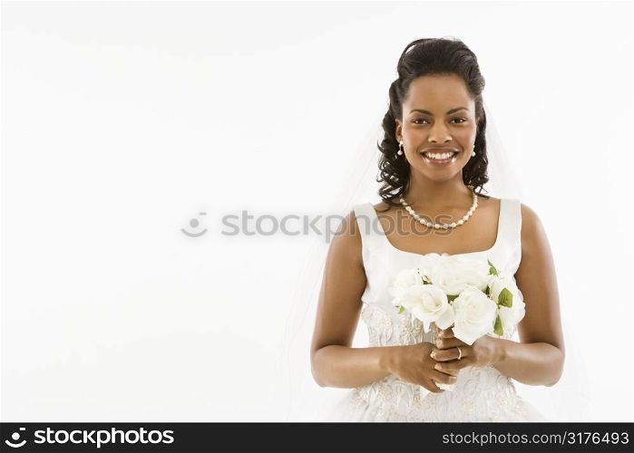 Mid-adult African-American bride holding bouquet on white background.