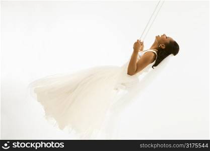 Mid-adult African-American bride swinging with white background.