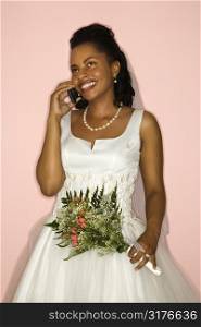 Mid-adult African-American bride talking on cellphone on pink background.