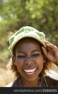 MId-adult African American female smiling with hand on cap and squinted eyes.