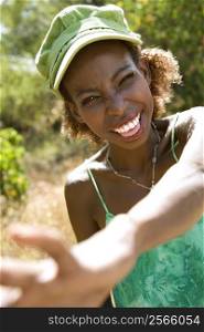 Mid-adult African American female smiling with hand reaching out towards camera.