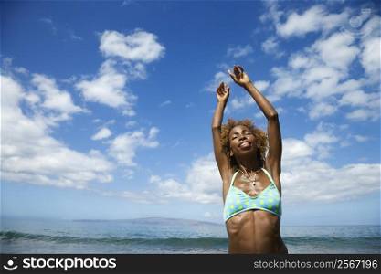 Mid-adult African American female stretching arms with clouds and ocean in background.