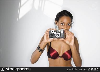 Mid-adult African American woman in bra holding up camera looking at viewer.