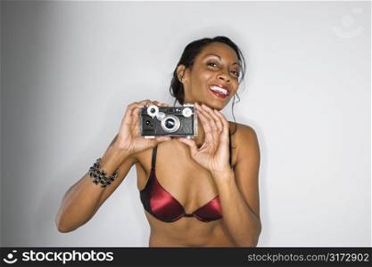 Mid-adult African American woman in bra holding up camera smiling and looking at viewer.