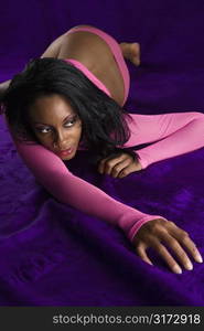 Mid-adult African American woman in hot pink underwear lying on purple background.