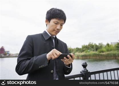 Mid adult Asian businessman using cell phone along river