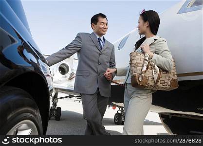 Mid-adult Asian businesswoman and businessman flirting outside of car and airplane.
