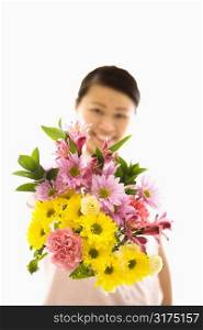 Mid adult Asian woman holding out bouquet of flowers.