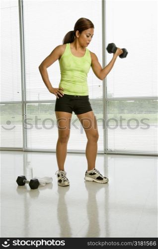 Mid adult Asian woman lifting dumbell with hand on hip.