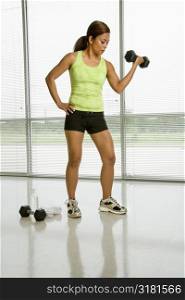 Mid adult Asian woman lifting dumbell with hand on hip.